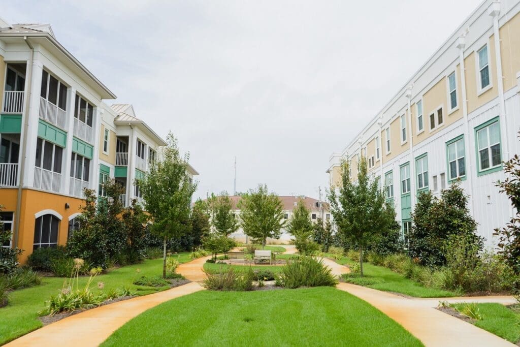 the-arbors-of-gulf-breeze-60-Large - Grace Management Lush garden pathways winding between modern, colorful senior living buildings, inviting a vibrant and active lifestyle.
