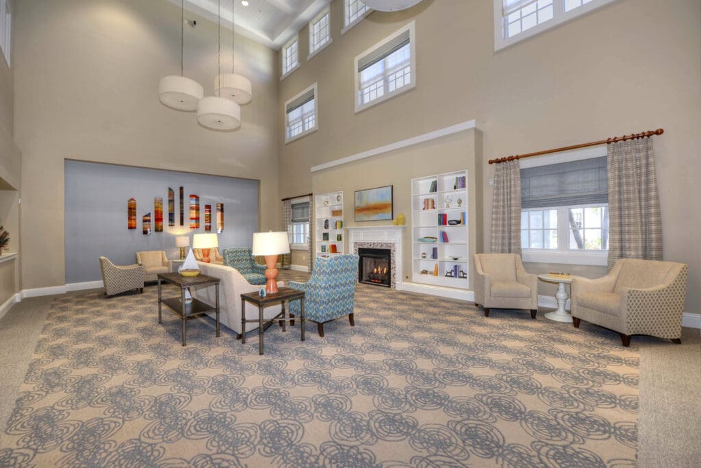 - Grace Management A sitting are with beige, blue, and green sofa chairs, fireplace, and white bookshelves that are built into the wall at Beach House, a senior living community.