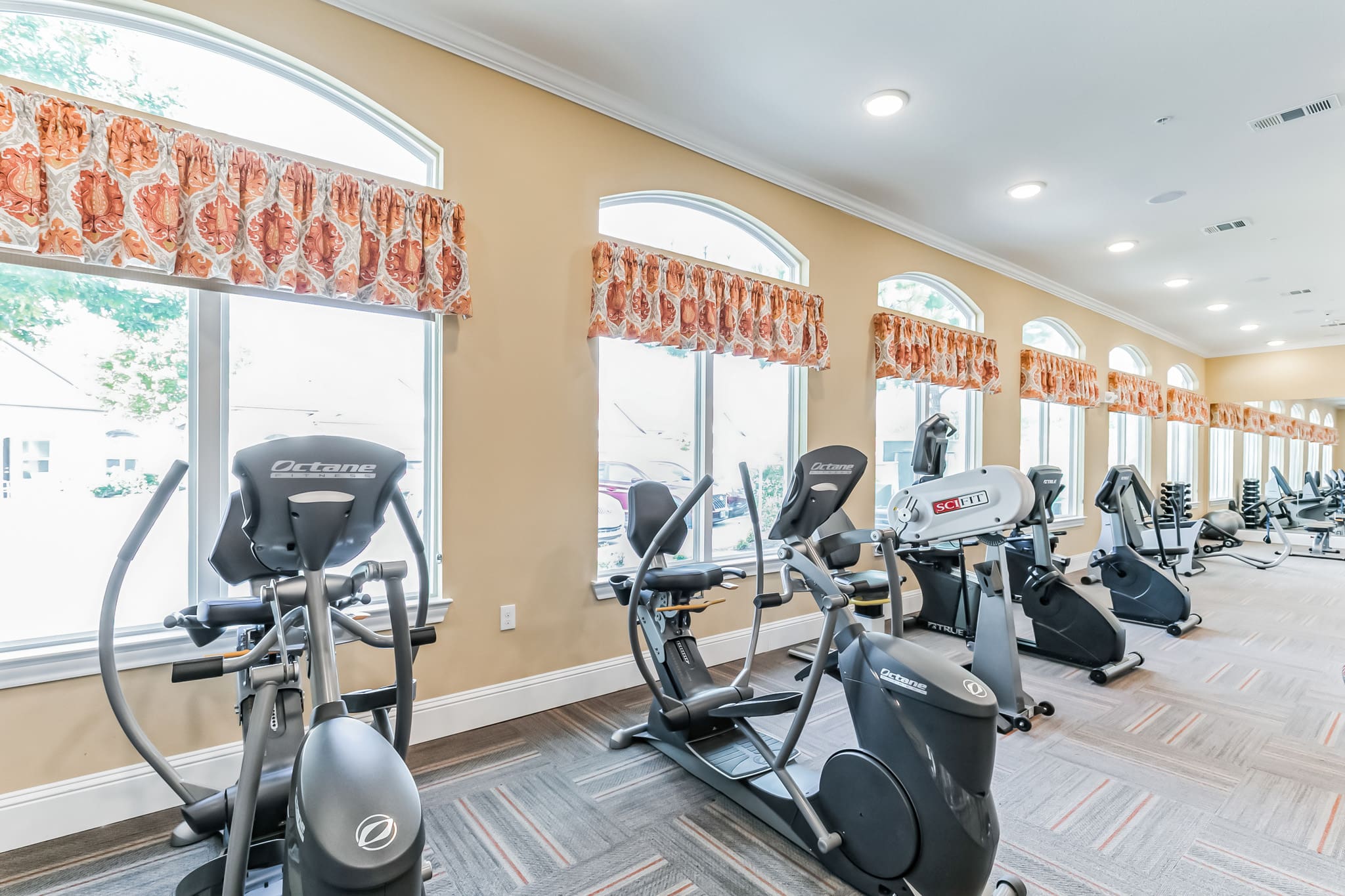 - Grace Management Interior image of the Woodhaven Village gym, equipped with lots of machinery and bright sunlight at Woodhaven Village, a senior living community near Spring, TX.