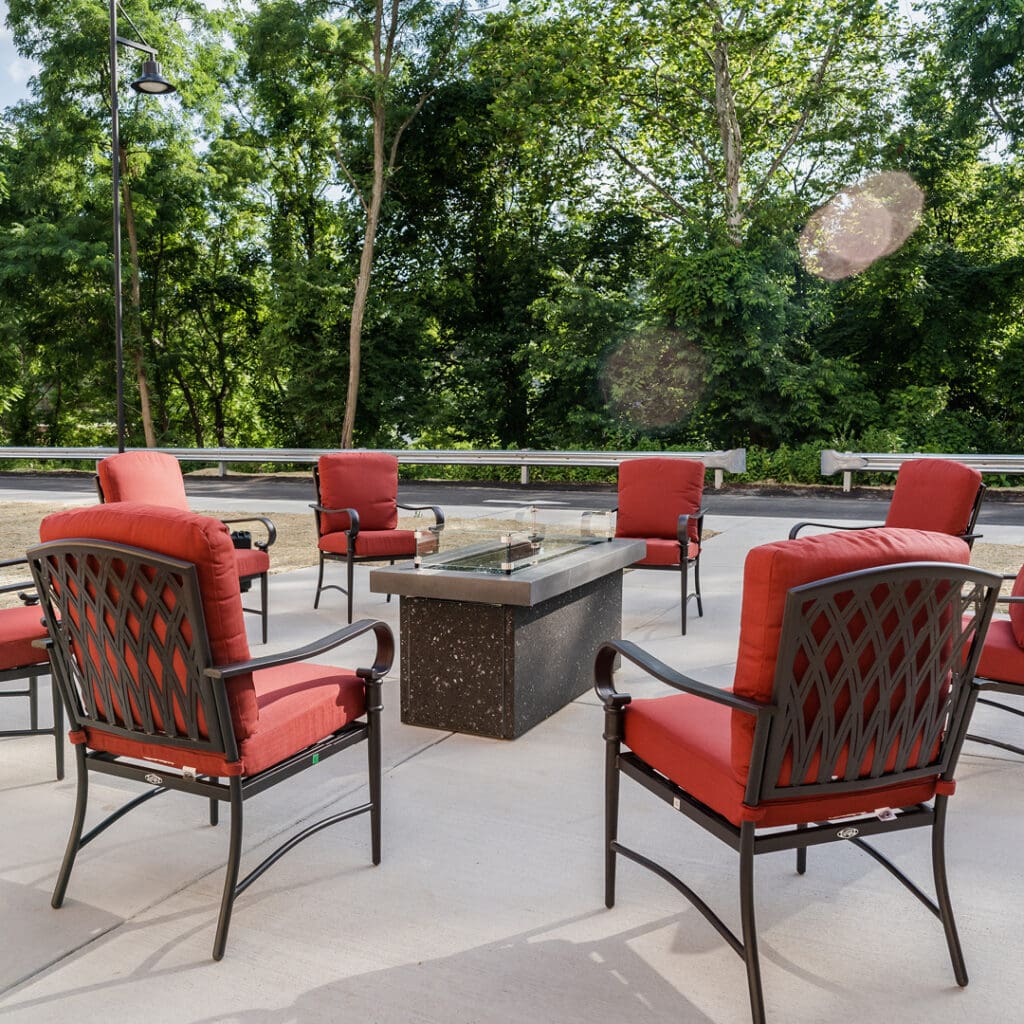 Red-cushioned chairs placed in a circle around a table outdoors, in front of many trees at The Residence at Whitehall, a great option for senior living in Allegheny County.