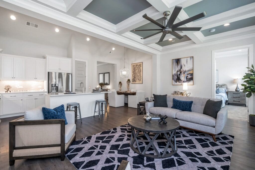 - Grace Management A photo of the large Cottage Main living room with a sofa, coffee table, fan, and a connected kitchen with a kitchen island and bar stools at Celebration Village Forsyth, a senior living community near Alpharetta, GA.