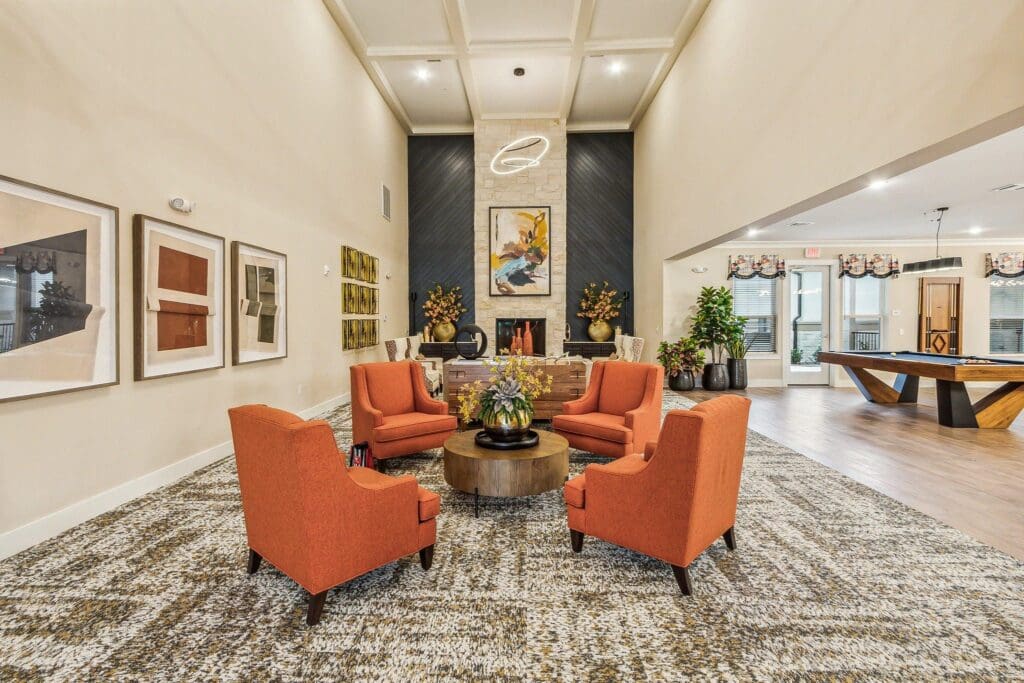 Interior living room with orange chairs and fireplace at The Lakes at Woodhaven Village, a retirement community near Huntsville, TX.
