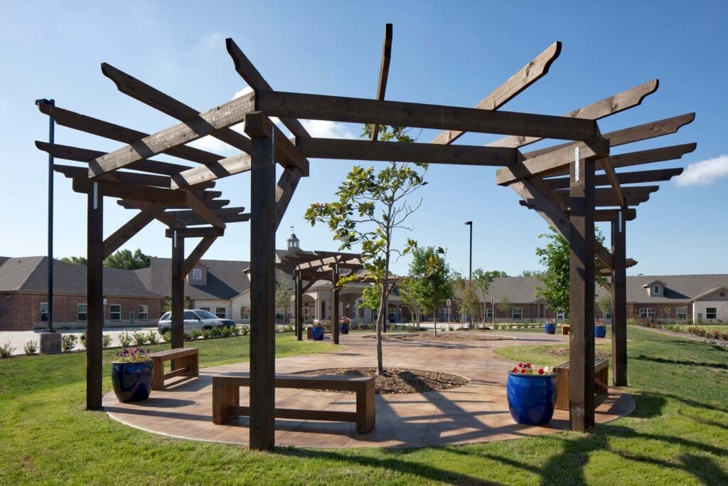 3D3A3882RT1RAB11inch-1-1024x683 - Grace Management A serene outdoor space with a wooden pergola, vibrant planters, and lush green grass, inviting relaxation and community engagement.