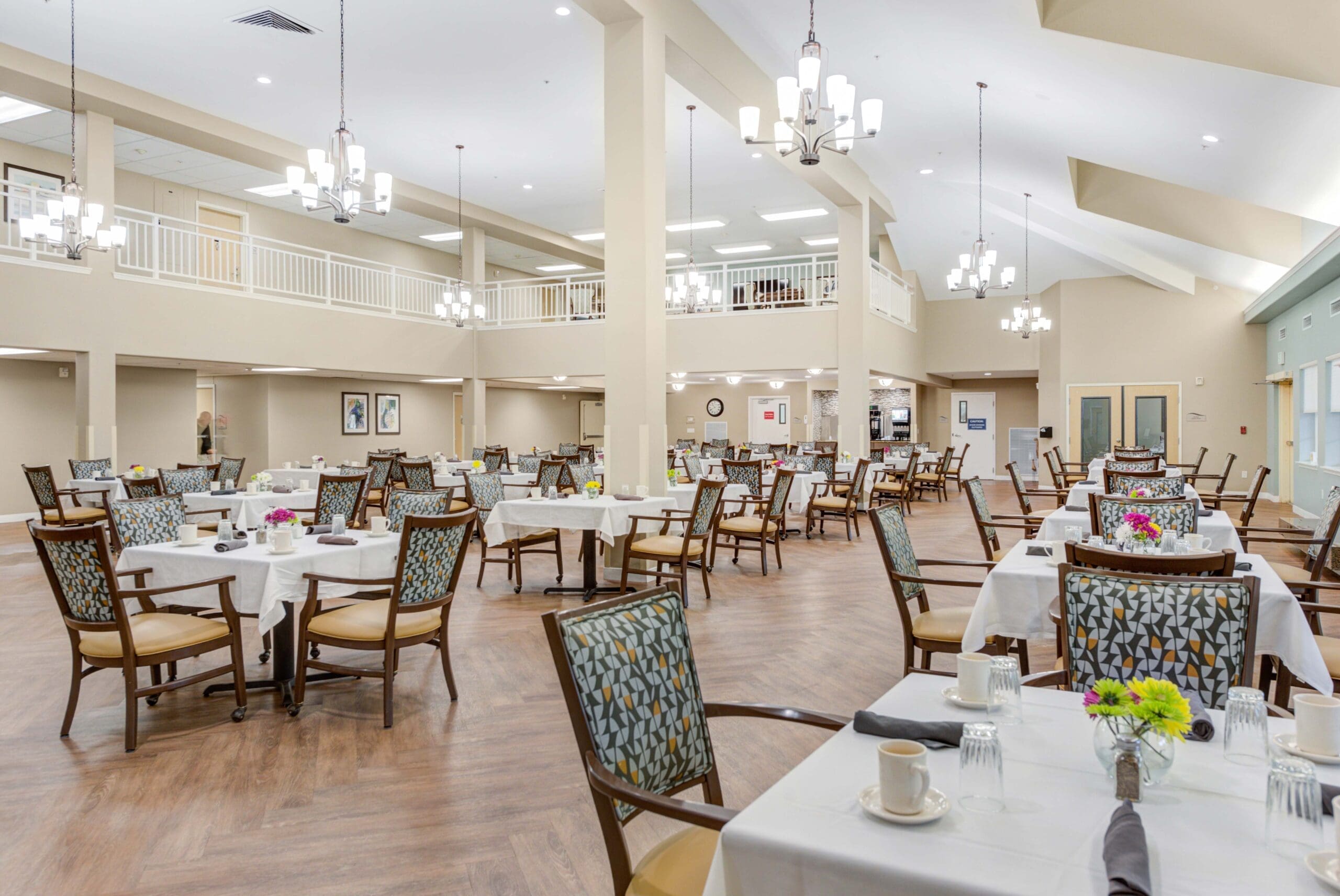 Interior image of Windward Palms' dining room. The room offers decorated tables, comfortable chairs, and luxurious chandeliers hanging from the ceiling at Windward Palms, a top choice for senior living in Delray Beach.