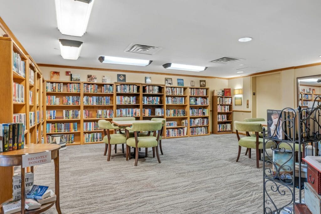 The library contains floor-to-ceiling bookshelves and reading tables at Town Village Vestavia Hills, a senior living community near Homewood, AL.