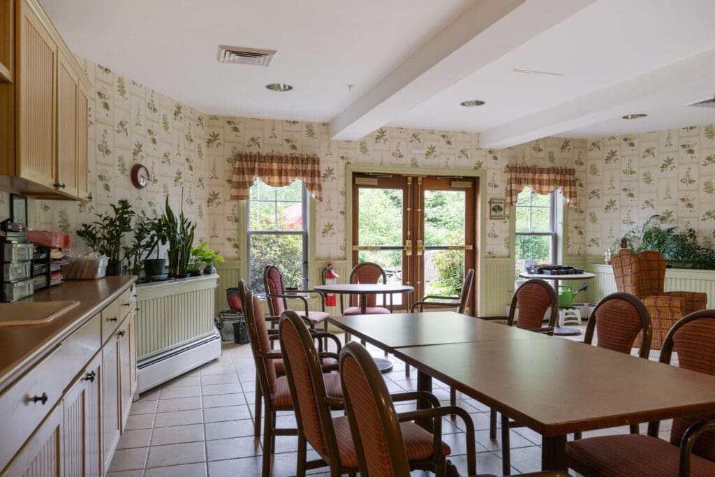 - Grace Management Cozy dining area with a large wooden dining table and beautiful natural light at Dirigo Pines, offering a retreat for residents enjoying senior living near Bangor, ME.