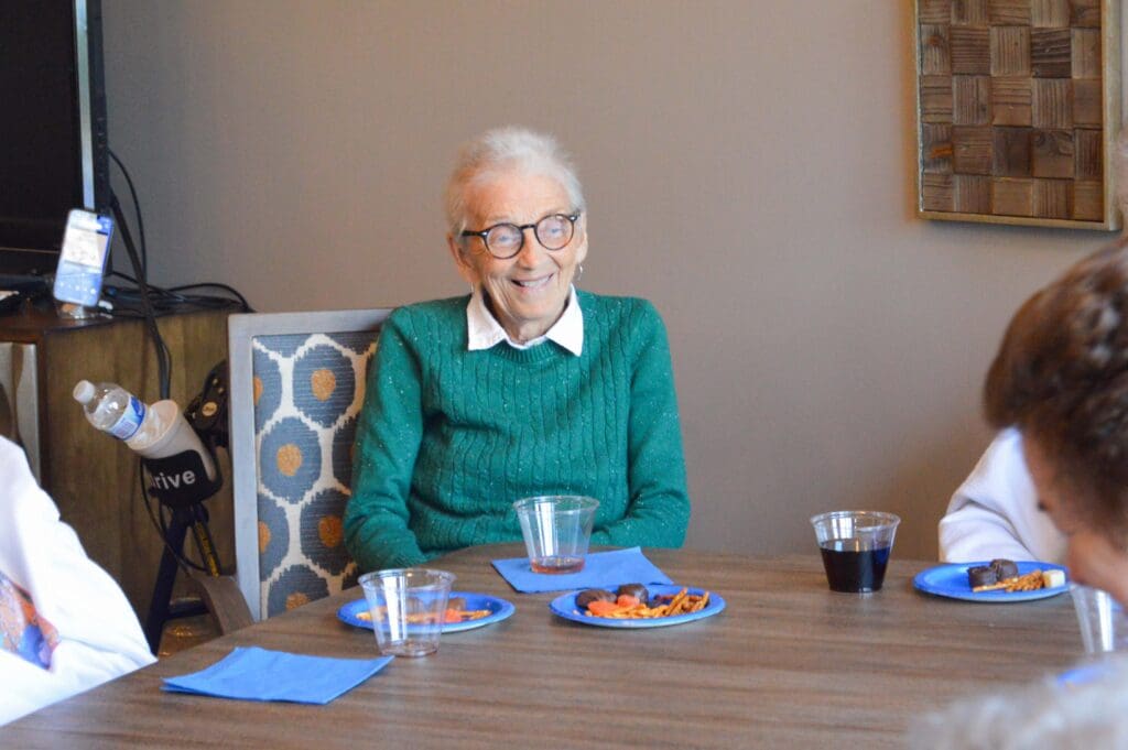 - Grace Management A smiling resident enjoys snacks and drinks at Inspirations of Mount Washington, highlighting the social atmosphere of senior living in Taylorsville.