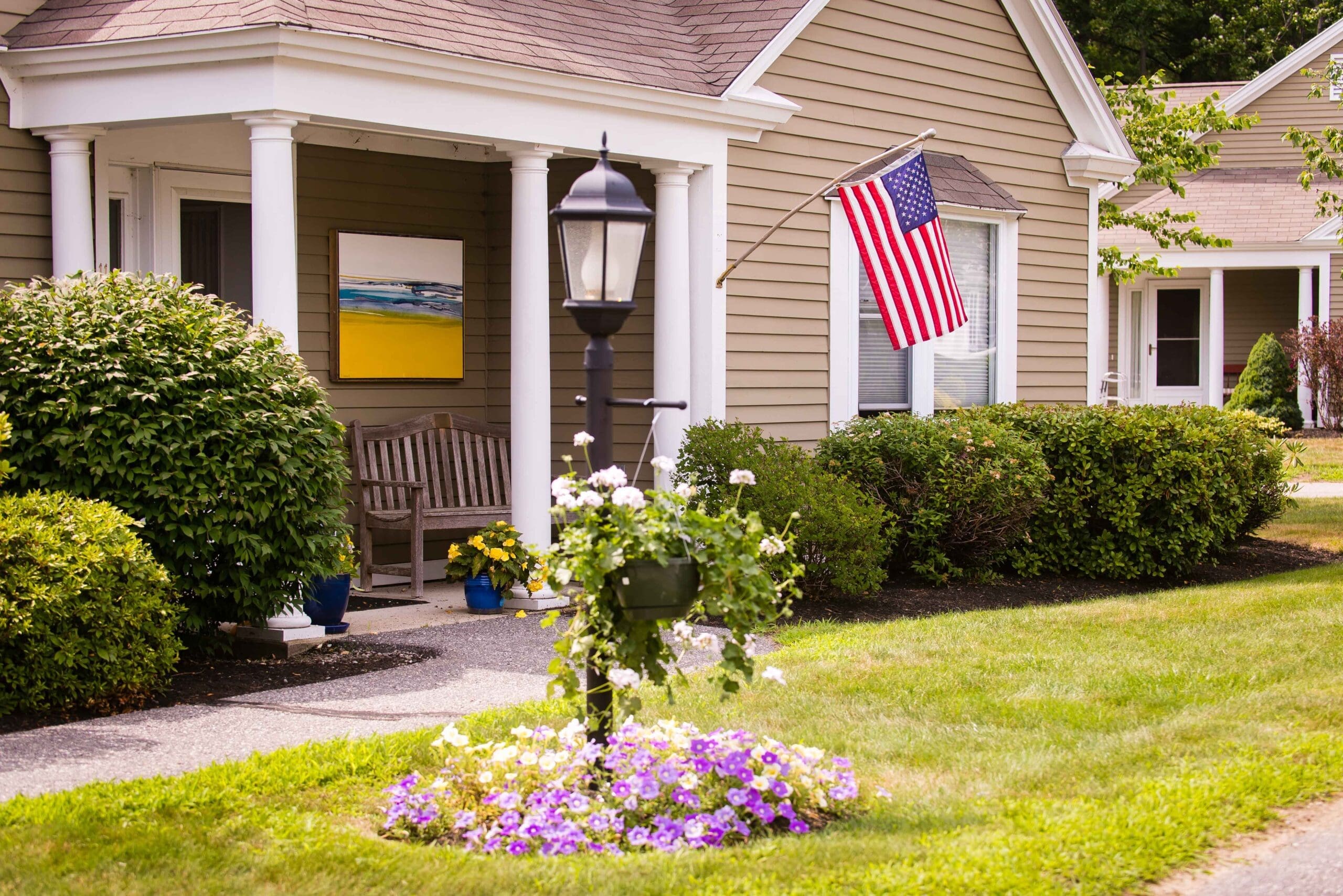 The Highlands community building with an American flag, a street light, a green lawn, and bushes in front of it at The Highlands, a premier senior living community near Lewiston, ME.