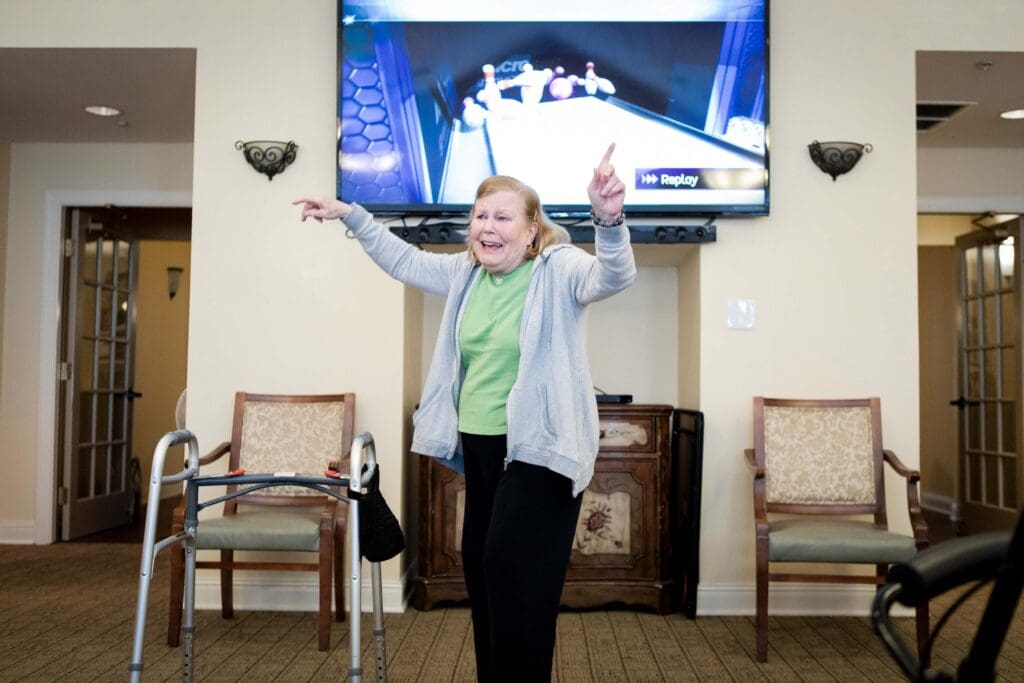 - Grace Management An older woman lifting her hands in the air as she's turned away from the TV, which displays a strike in the video game of bowling at Northgate Park.