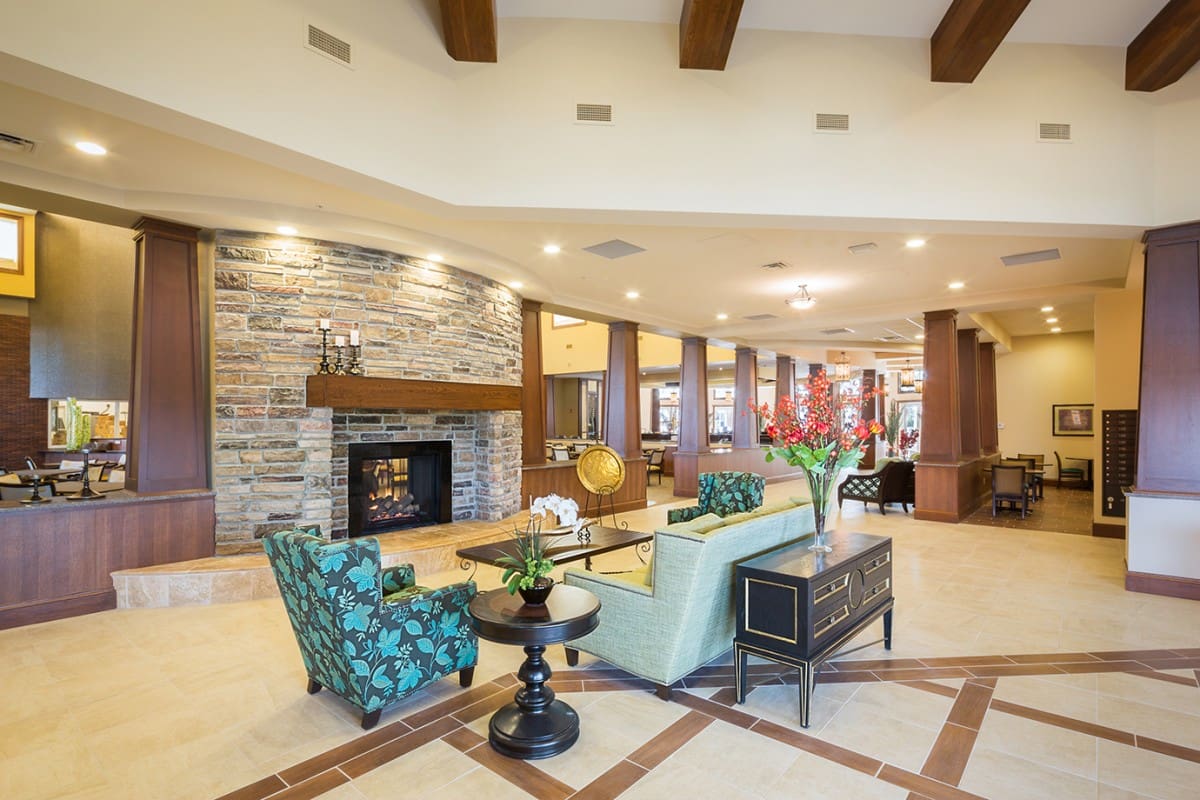 - Grace Management The grans lobby area with a light blue couch, blue sofa chairs, side tables with vases of flowers on them, all in front of a fireplace.