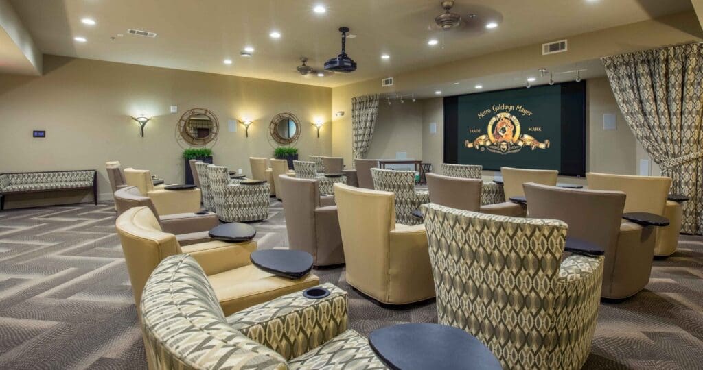 A movie theater room with light yellow, brown, and patterned sofa chairs positioned in front of the projector that's displaying the Metro Goldwyn Mayer lion intro.