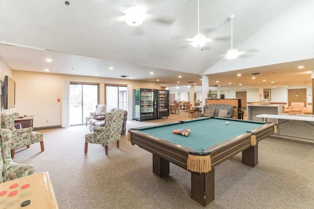 - Grace Management A lounge room with a billiard table in the middle, flower-patterned sofa chairs, a vending machine, and a grey couch at Northgate Park.