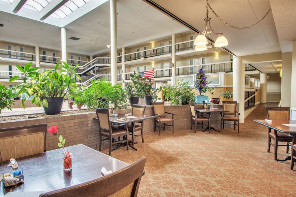 - Grace Management A dining area with brown tables and chairs, and a single pink flower sitting in a little vase on each table at The Atrium of Belleville.