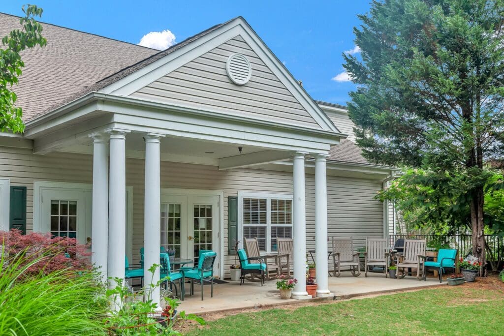 Covered patio with rocking chairs and garden seating at The Willows of Easley, showcasing the peaceful setting of senior living near Greenville, SC.