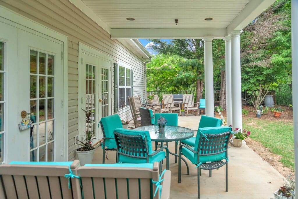 - Grace Management The Willows of Easley outdoor patio with turquoise cushioned chairs surrounding a glass coffee table, and a row of brown reclining chairs.