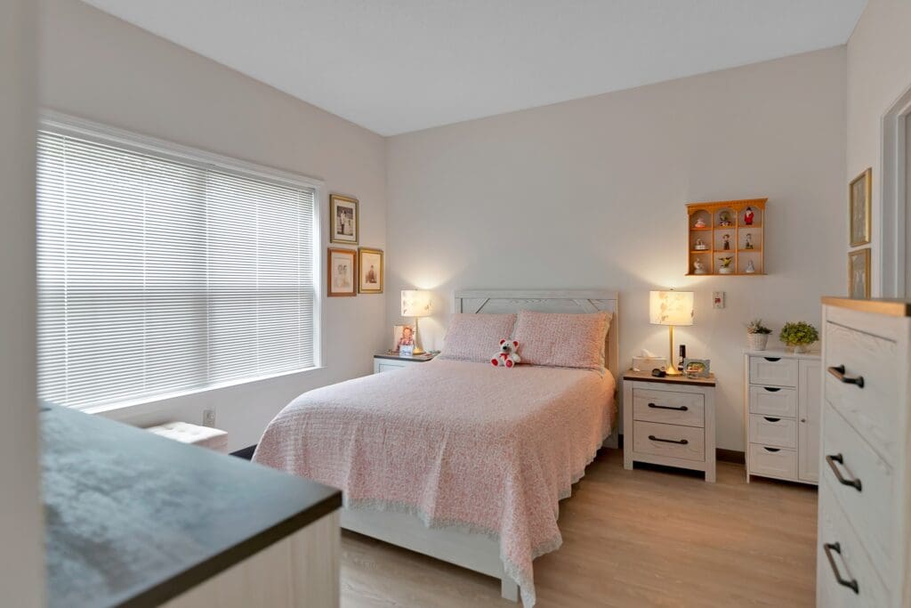 - Grace Management A bedroom with a Queen-sized bed and pink bedding, two bedside tables with lamps, wall art, and two white dressers.