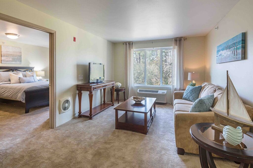 Interior living room at Augustine Landing in Florida with a brown couch, brown coffee table, brown TV stand, a TV, and an open door that leads to the bedroom.