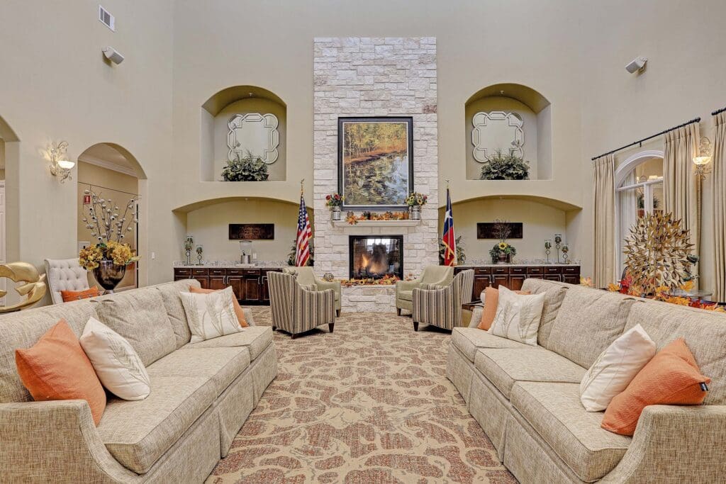 Interior image of Woodhaven Village's common area. There are comfortable couches, chairs, and a roaring fireplace.