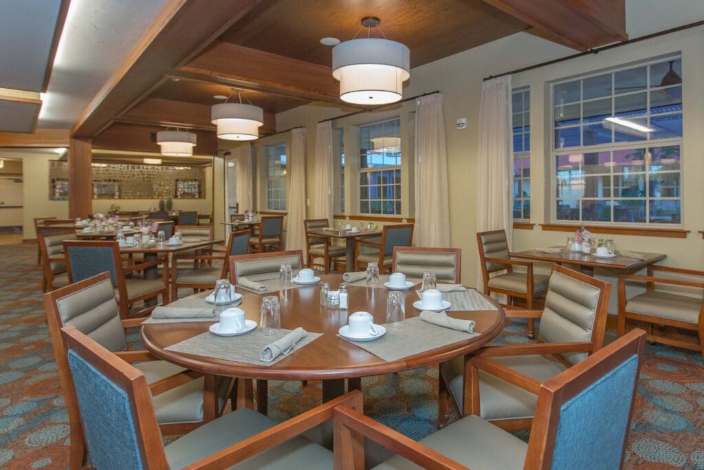 The Ranch Estates of Tucson dining area with circular brown tables, blue cushioned chairs, gray placemats and napkins, white cups, and glasses.