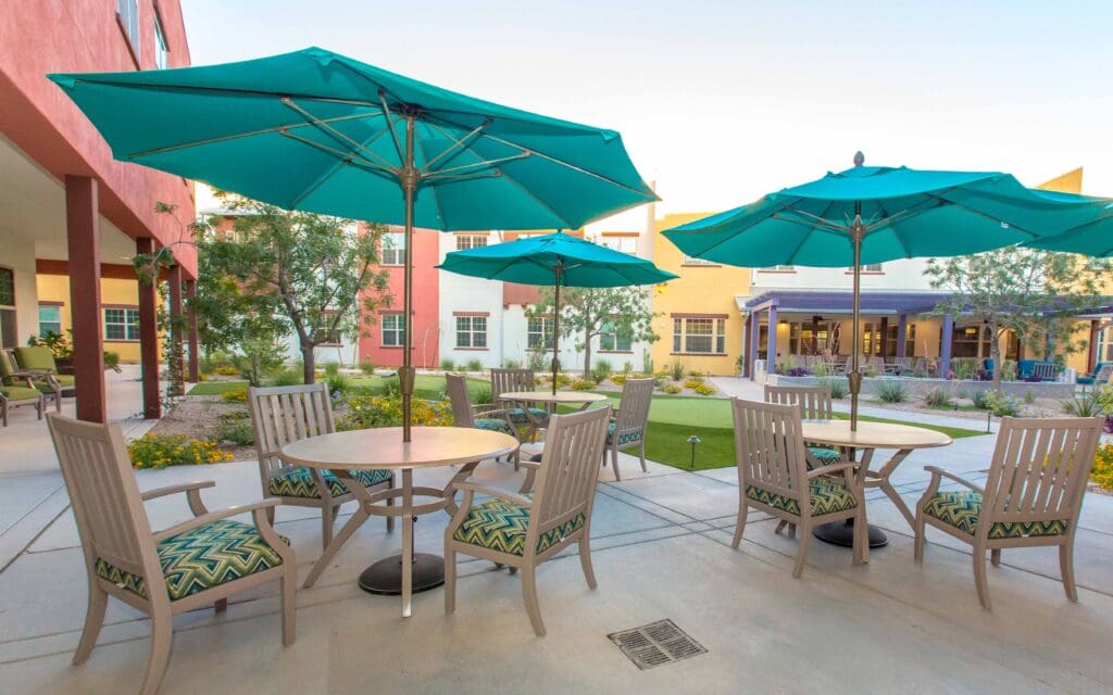 The Ranch Estates of Tucson courtyard with beige tables and chairs and blue umbrellas.