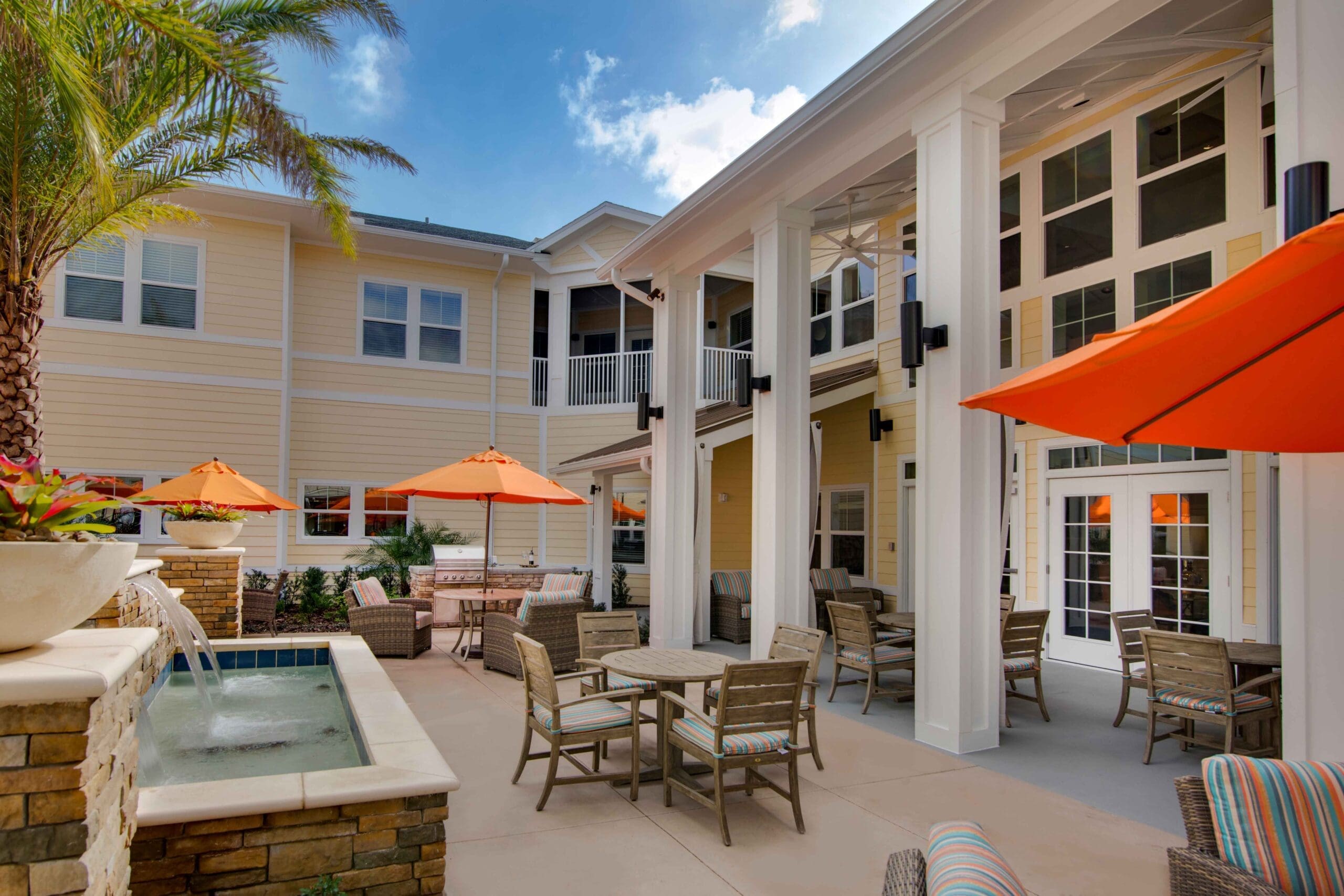An outdoor patio with wicker furniture, umbrellas, and a water feature at The Summit of Winter Garden, a senior living community near Clermont, FL.