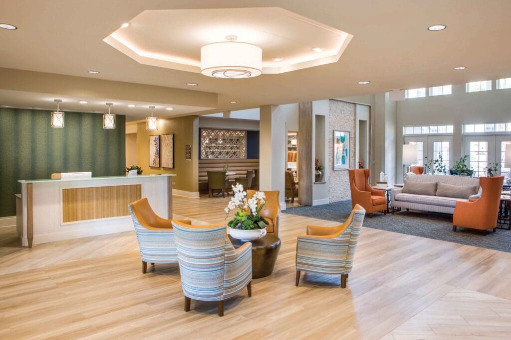 A sitting area with orange striped sofa couches around a round table with flowers on it, a reception area, and a gray couch with orange sofa chairs at The Summit of Winter Garden, an independent and assisted living community near Orlando.