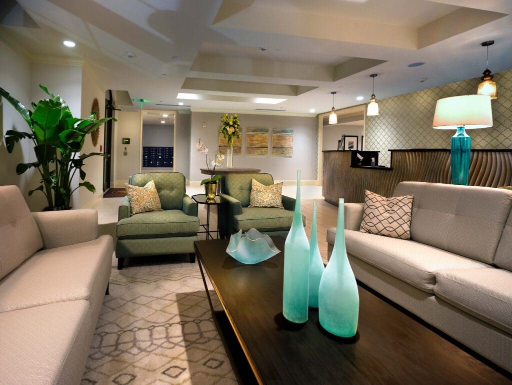 Three turquoise vases and a bowl sitting on top of a brown coffee table in the middle of two beige couches and in front of two green sofa chairs with throw pillows on them.