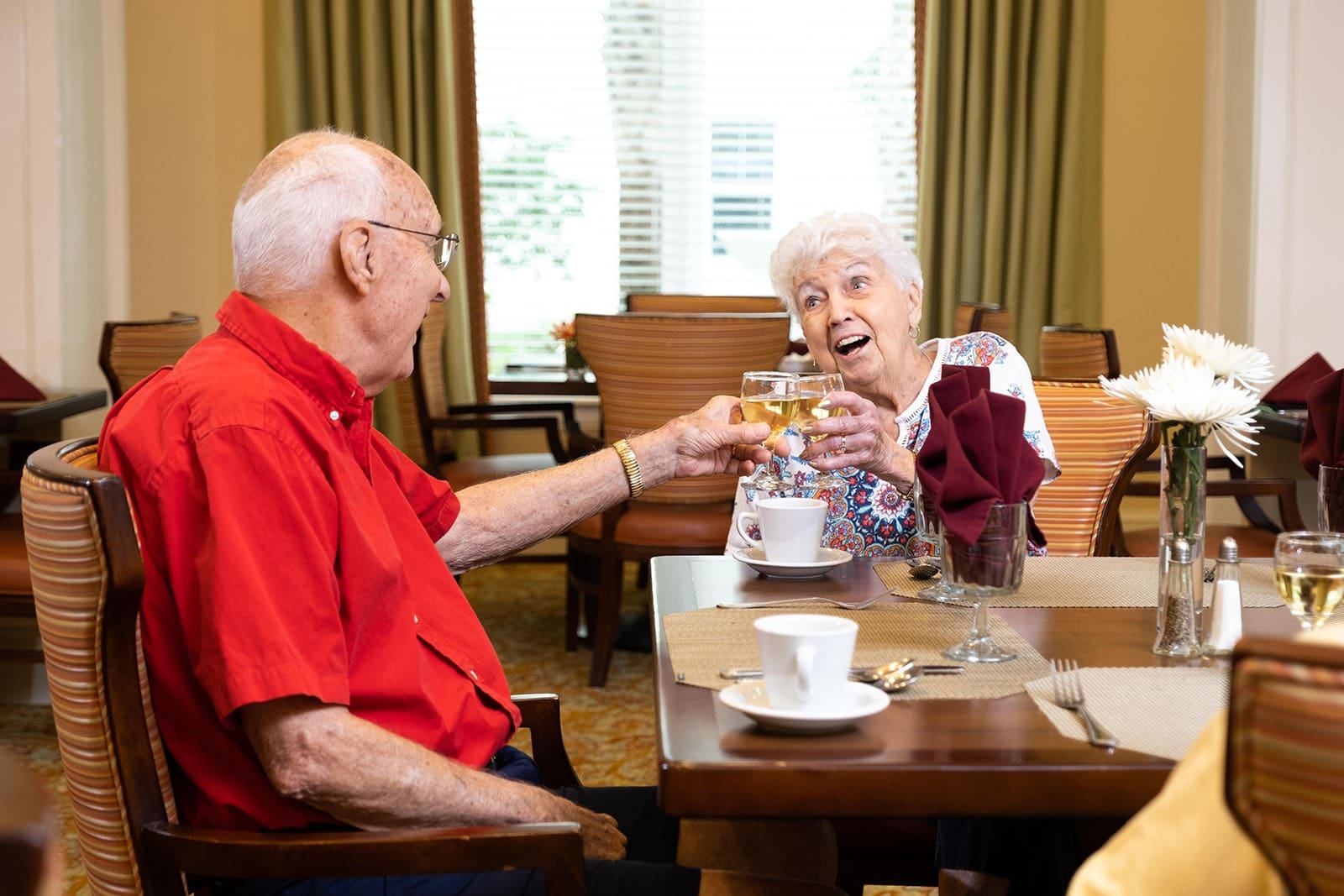 A happy resident toasting with a friend in the dining room atThe Summit of Lakewood Ranch, a top senior living choice.