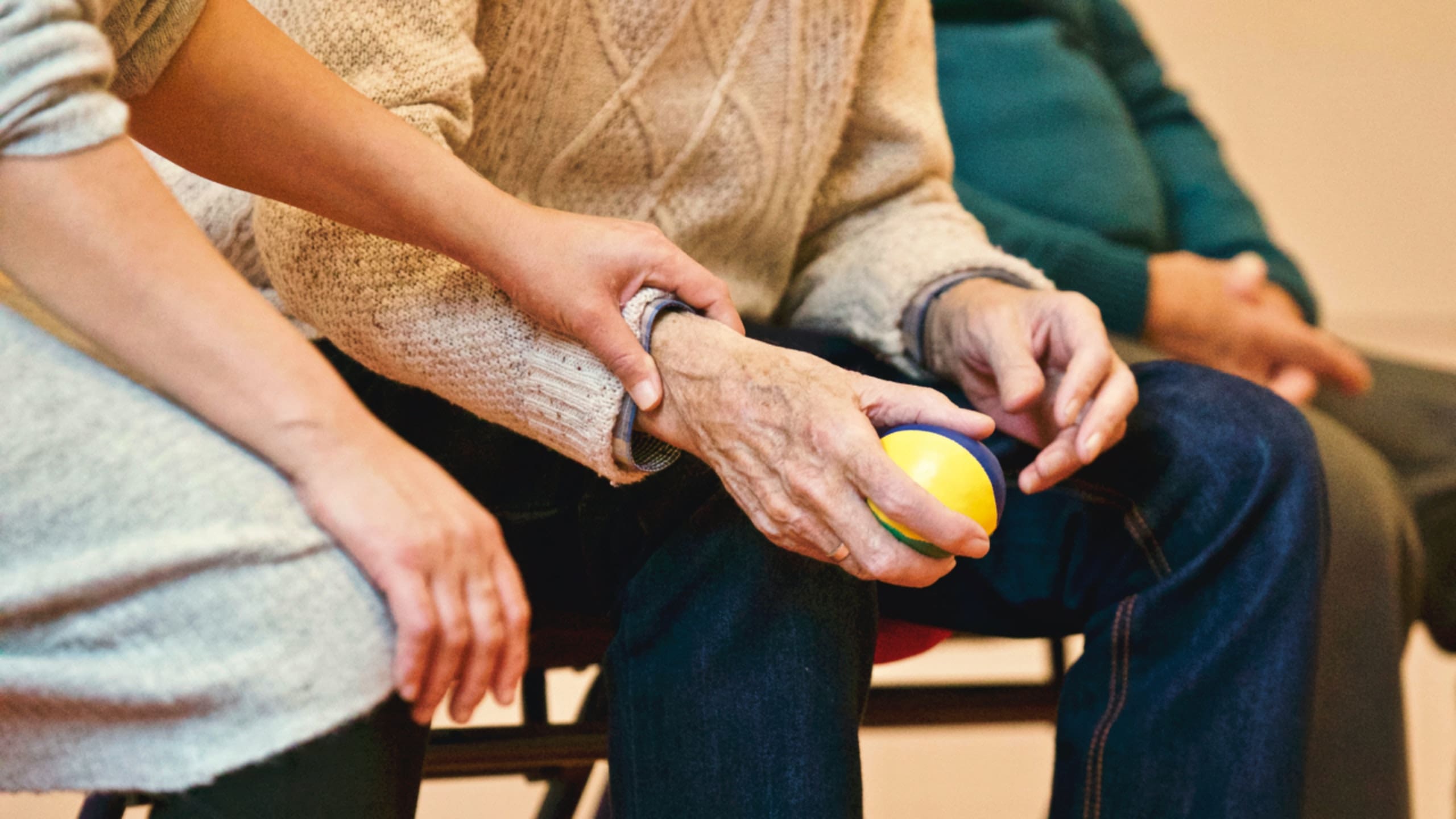 - Grace Management An up-close shot of an older person's hands holding a colorful stress ball, and a pair of younger hands holding the older person's ones.