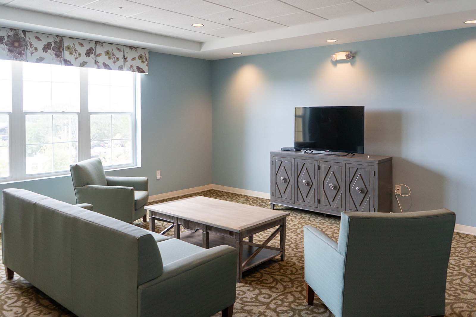 Interior image of The Arbors of Gulf Breeze television room. Senior living social area, decorated in muted blues, greens, and browns.