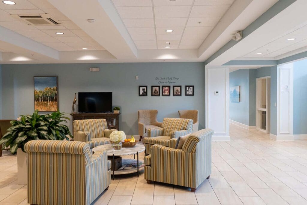 - Grace Management Interior image of The Arbors of Gulf Breeze lobby with comfortable furniture, free snacks, and lush green plants. The walls are decorated with photos of Gulf Breeze residents who served in the Vietnam War, as well as a television for entertainment and books for reading.
