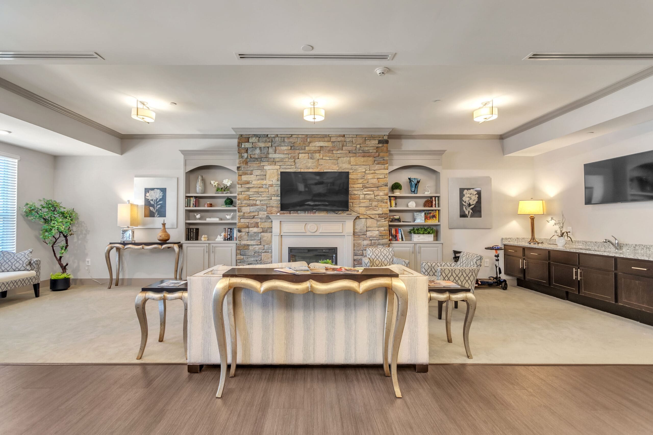 - Grace Management A room with two TVs, fireplace, couch, sofa chairs, multiple desks, a sink, and brown cabinets at Celebration Village Forsyth, a senior living community near John's Creek, GA.