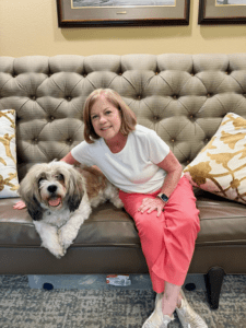 Happy senior woman with her adult daughter at home - Grace Management Two women with silver hair share a joyful moment, smiling and leaning close in a warm, inviting setting filled with greenery.