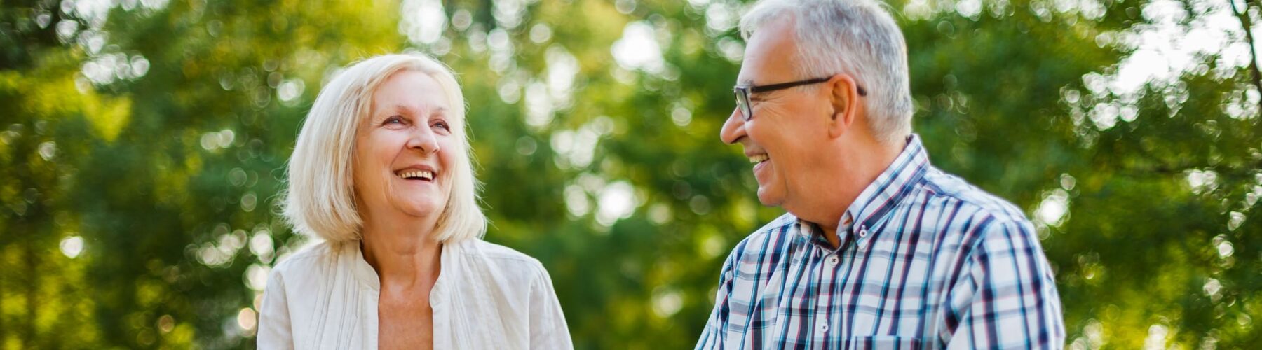 Two seniors enjoy a joyful conversation on a park bench, surrounded by lush greenery and a warm, inviting atmosphere.