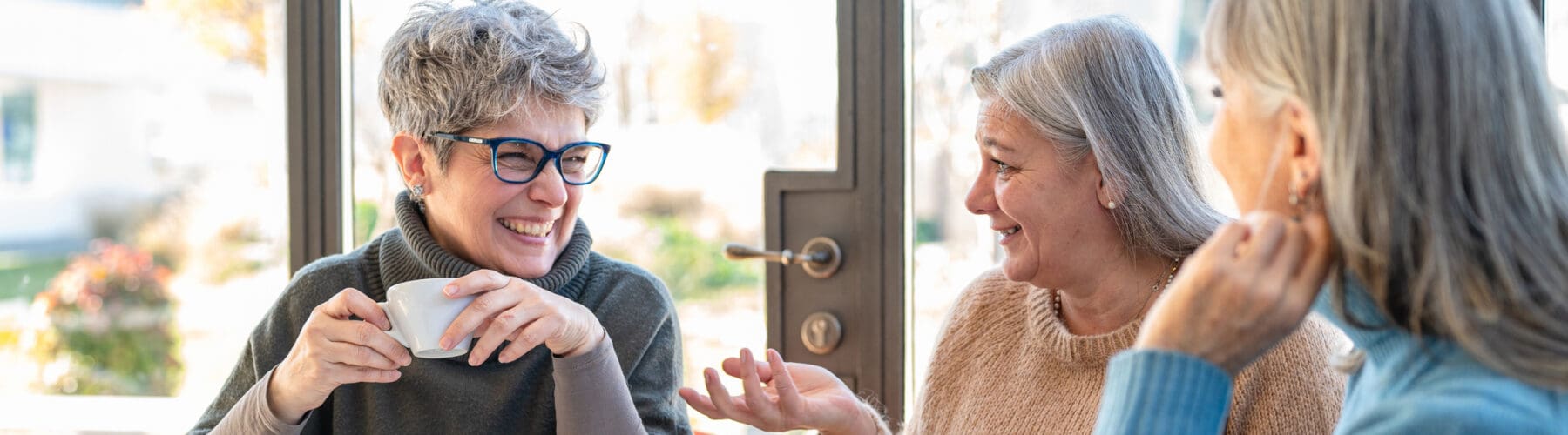 Three women enjoy coffee and conversation in a bright, welcoming café, showcasing a vibrant social atmosphere.