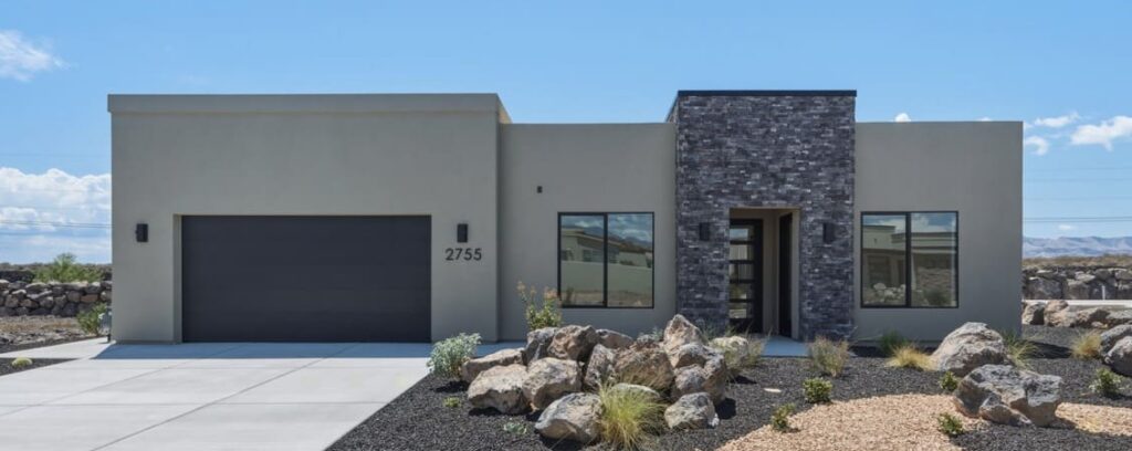 Stylish modern home with stone accents, landscaped rocks, and a welcoming entryway under a clear blue sky.