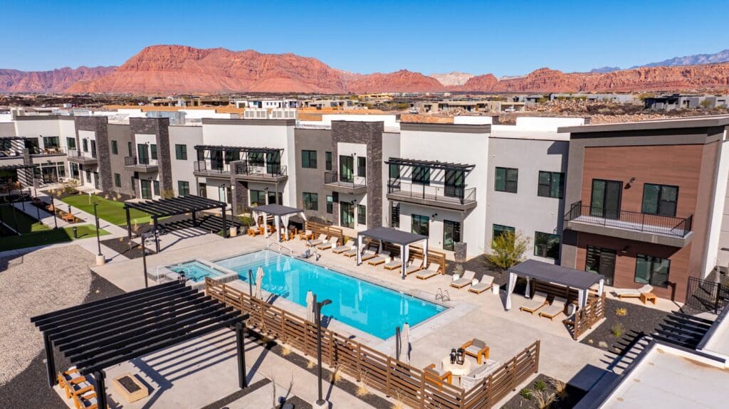 Luxurious senior living community with a sparkling pool, elegant cabanas, and stunning mountain views under a clear blue sky.