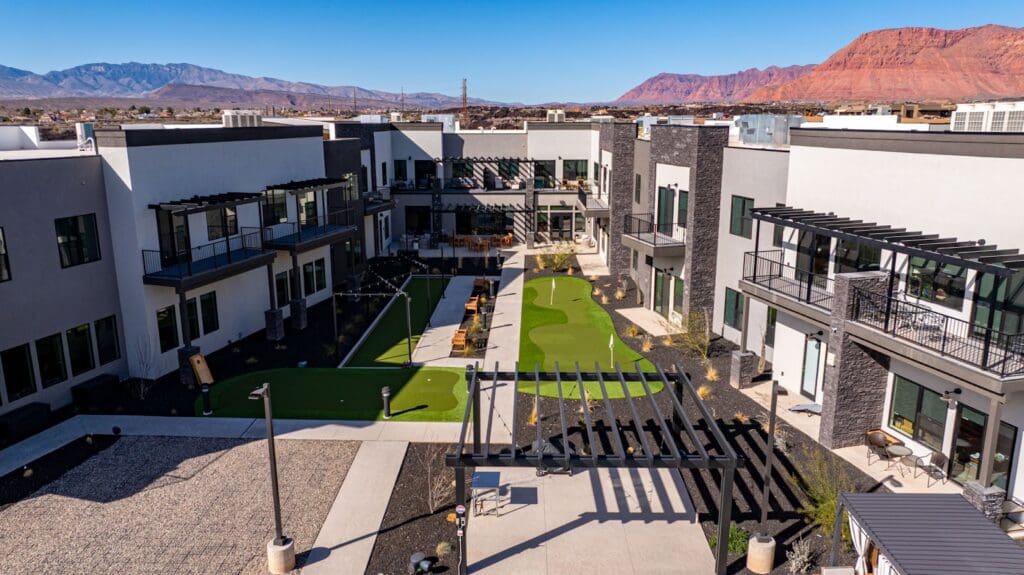 Expansive courtyard with green space, outdoor seating, and modern residences against a stunning mountain backdrop.