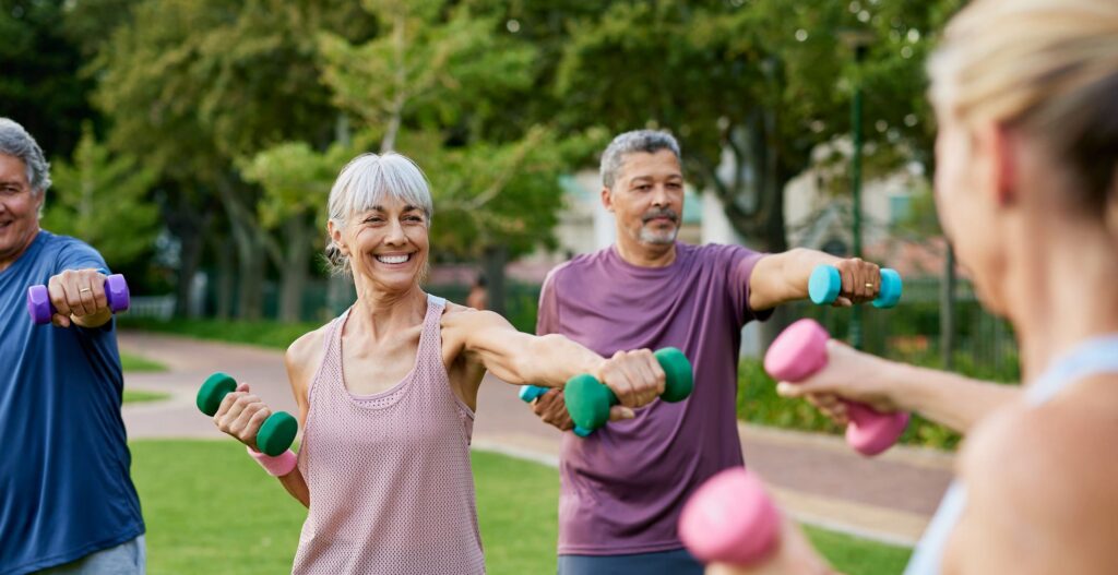 Seniors engaging in a joyful outdoor fitness class, lifting colorful dumbbells, surrounded by lush greenery.