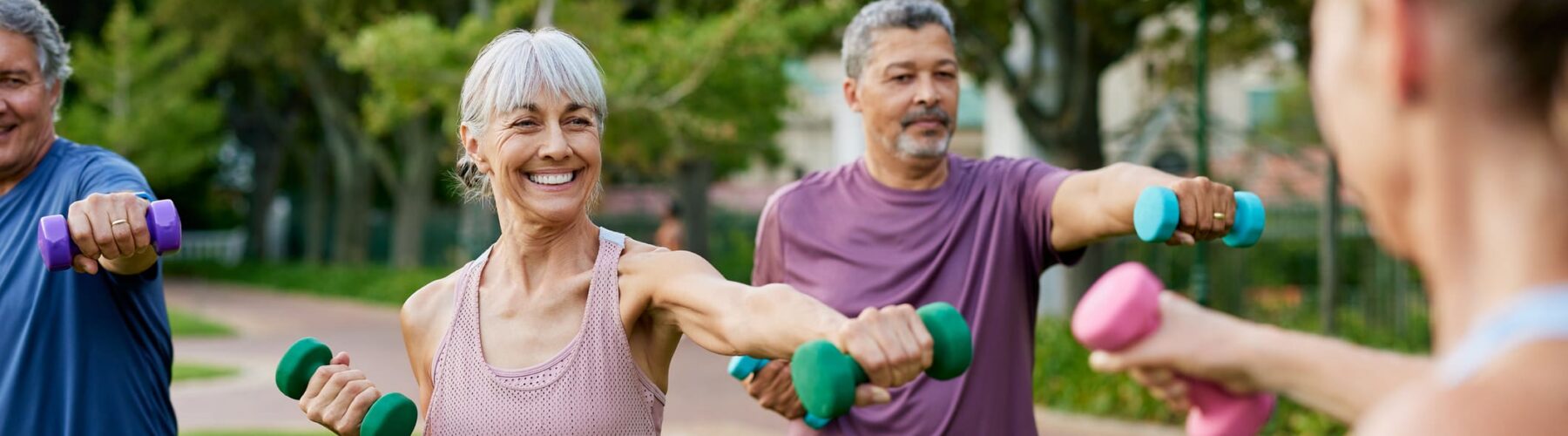 Seniors engaging in a joyful outdoor fitness class, lifting colorful dumbbells, surrounded by lush greenery.