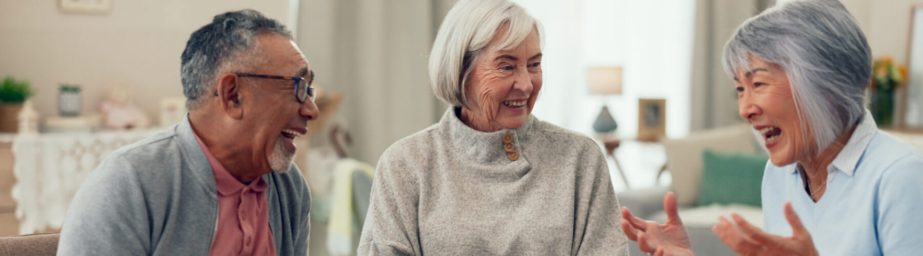 Three seniors enjoying a lively conversation over tea and snacks in a bright, inviting living space.