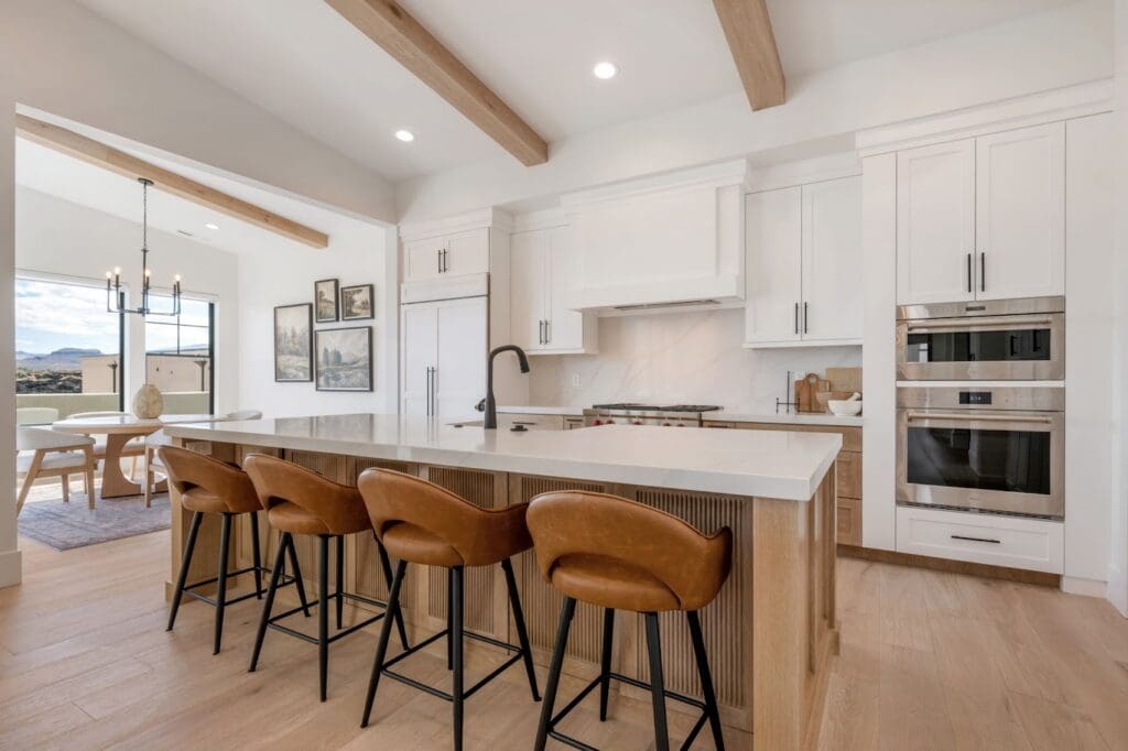 Modern kitchen featuring sleek cabinetry, a spacious island with leather stools, and large windows showcasing beautiful views.