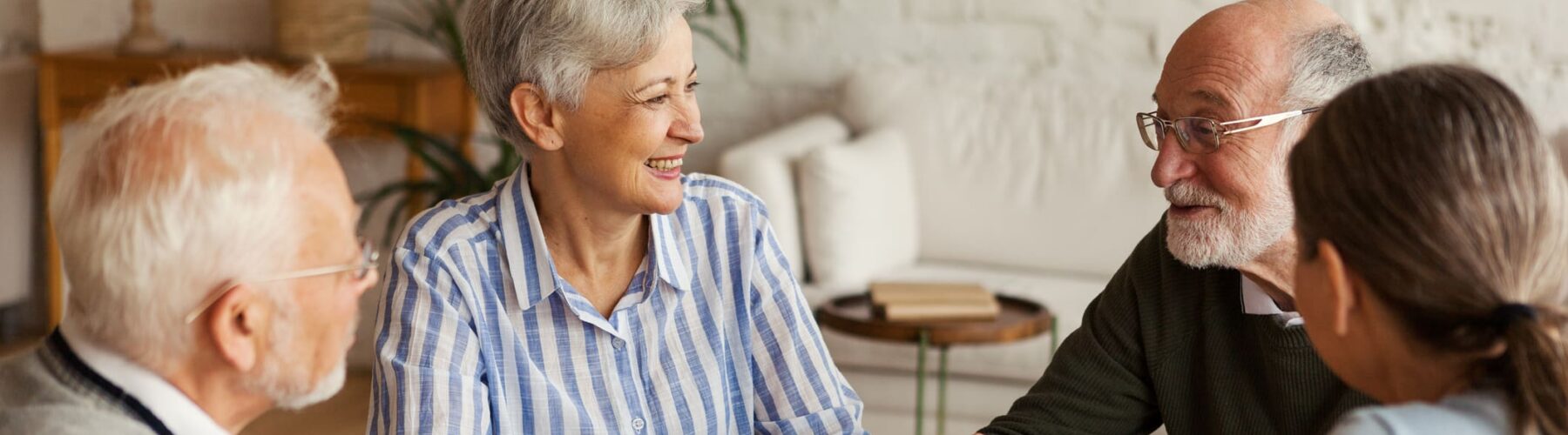 Seniors enjoying an engaging conversation around a wooden table in a bright, inviting living space.