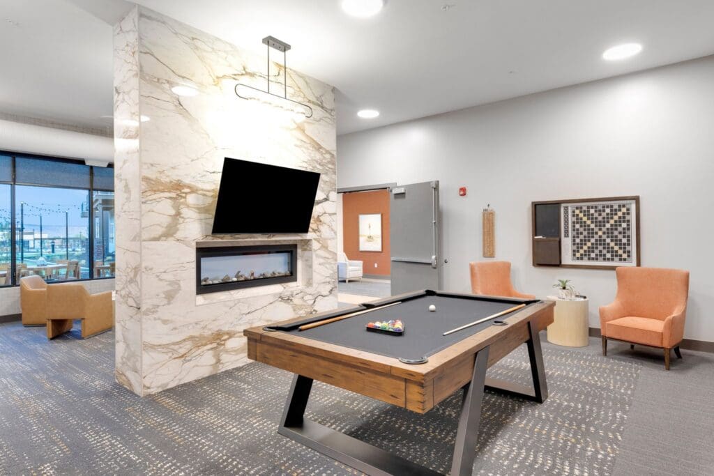 Modern recreational lounge featuring a billiards table, cozy seating, elegant decor, and large windows with scenic views.