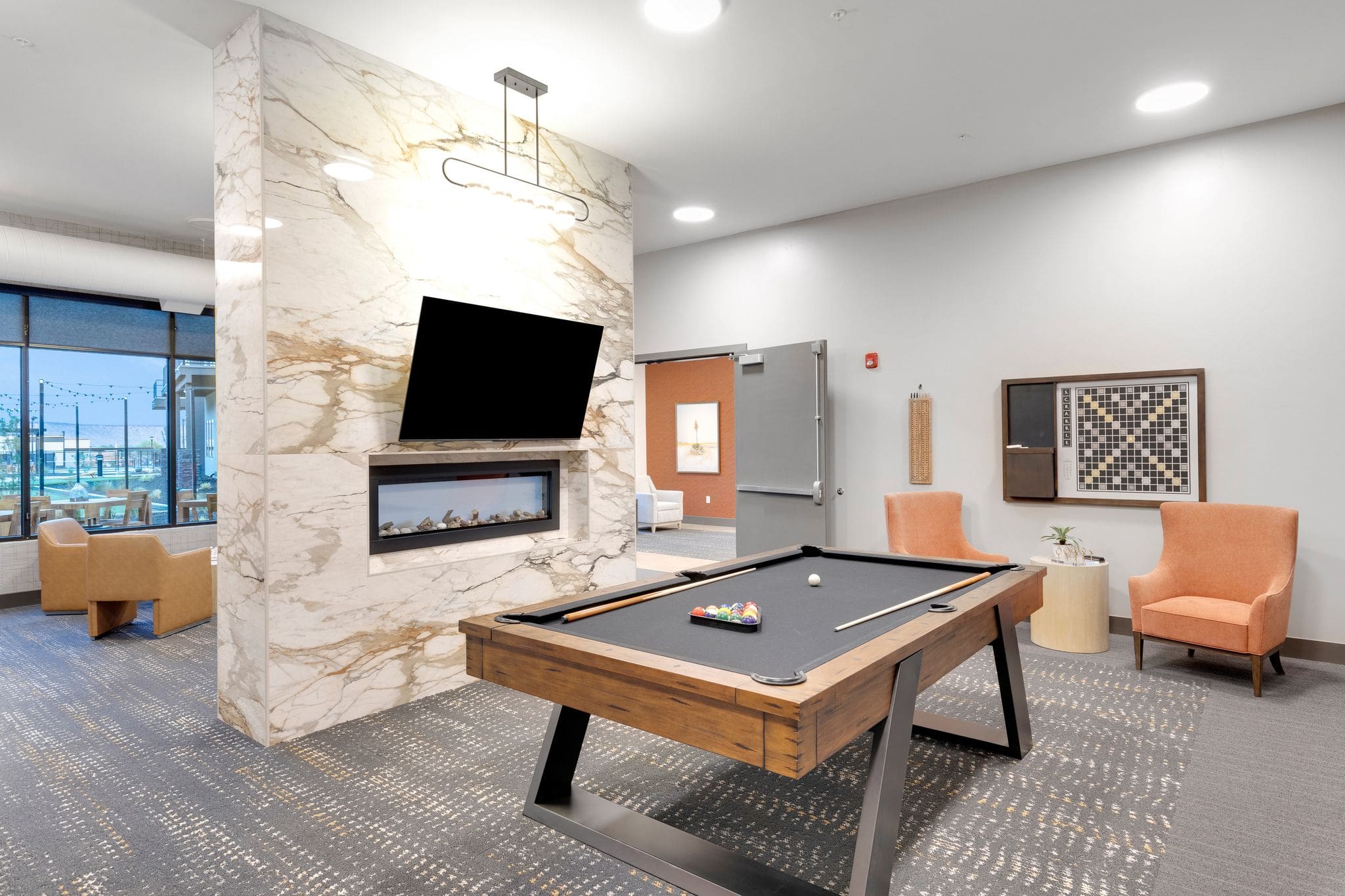 Modern recreational lounge featuring a billiards table, cozy seating, elegant decor, and large windows with scenic views.