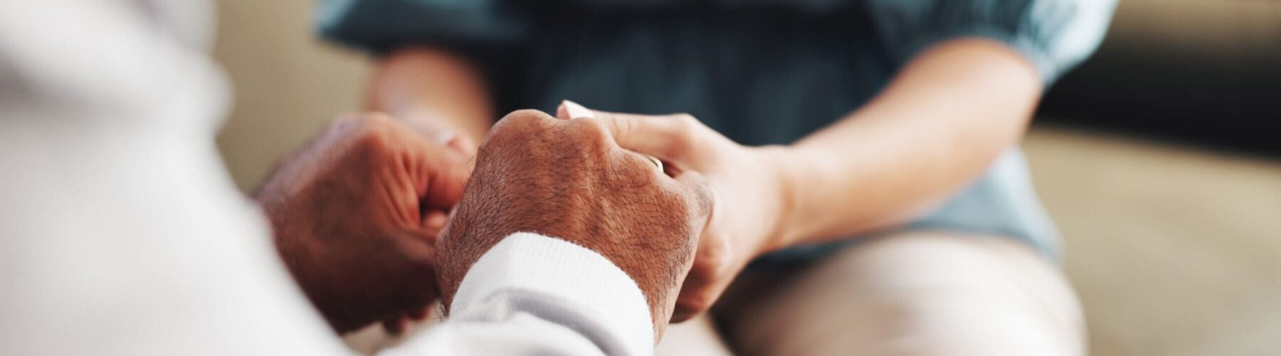Hands of an older adult and a caregiver clasped together, symbolizing compassion and supportive connection in a serene setting.