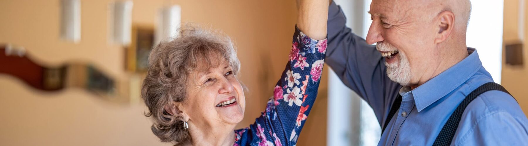 Happy senior couple dancing together at home - Grace Management Joyful couple dancing together indoors, celebrating companionship in a warm, inviting atmosphere.