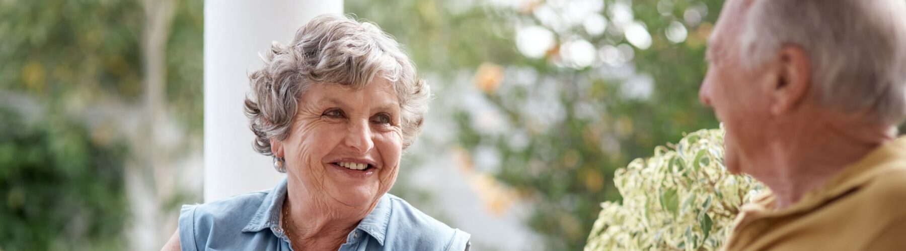 Seniors enjoying vibrant conversation and coffee on a sunny patio, surrounded by lush greenery and cozy seating.