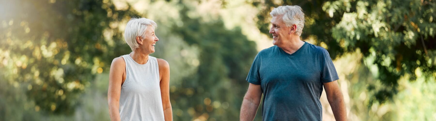 Older couple walking happily together with a golden retriever on a sunny, tree-lined street.