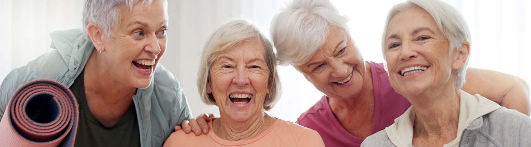 Yoga class and face of senior happy people for retirement exercise club membership and community wellness Pilates friends group portrait and elderly women at training fitness and workout studio - Grace Management Four joyful senior women, holding yoga mats, share laughter and companionship in a bright, inviting setting.